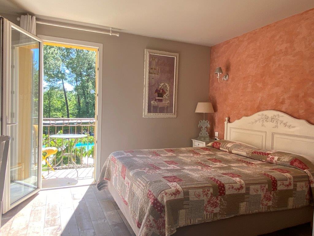 Bed and side table of bedroom with open door to terrace at Hotel Les Sables d'Ocre