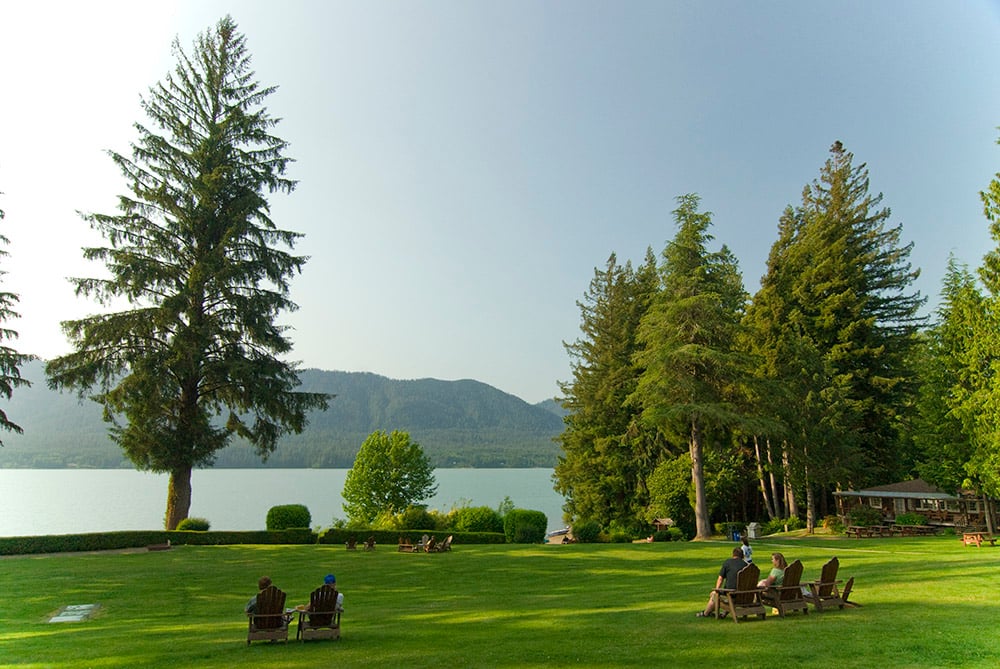 Lake Quinault Lodge exterior lawn down to lakefront with people sitting in wooden lounge chairs