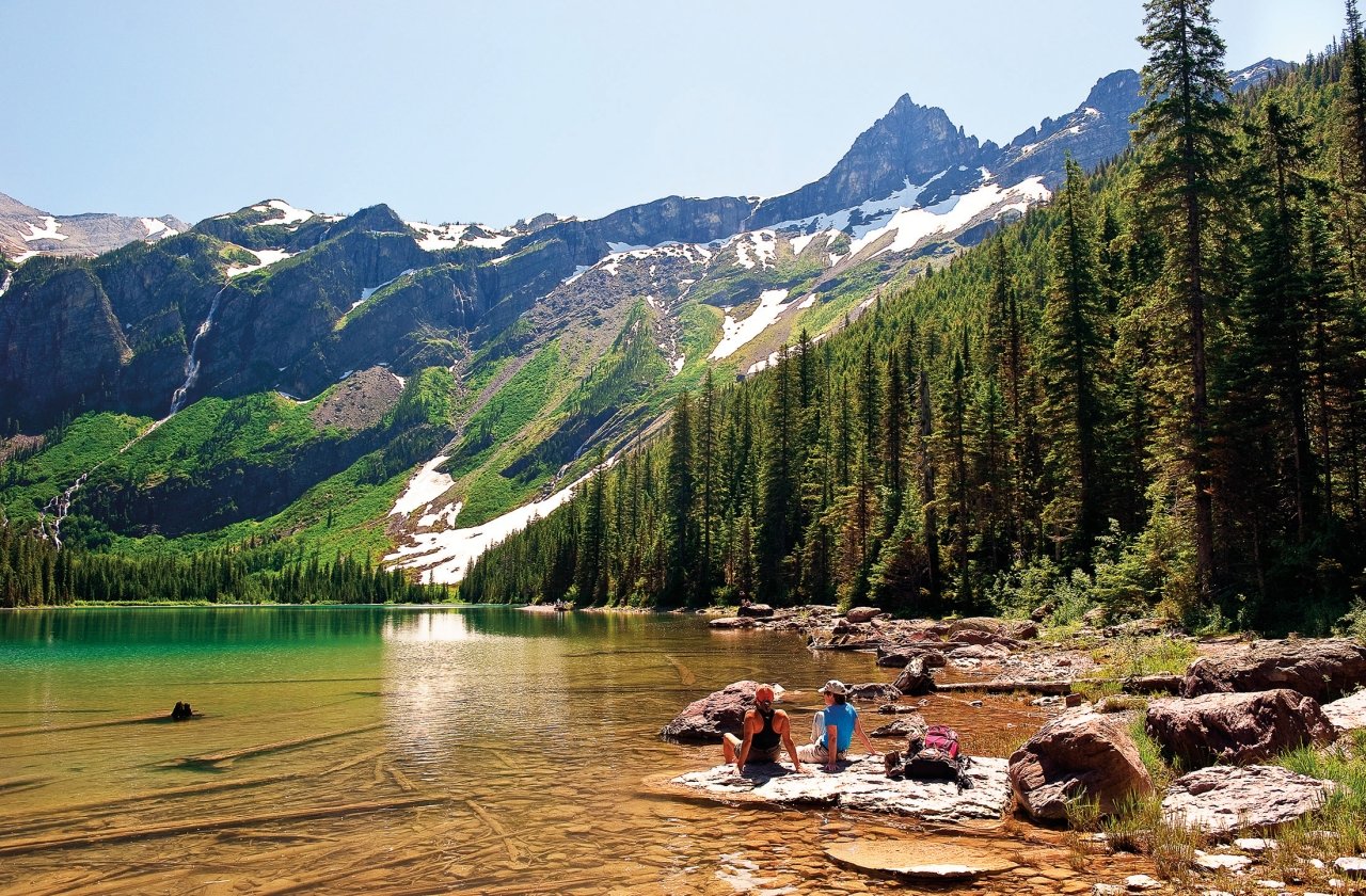 Rear view of two women sitting on a rock and watching the mountains