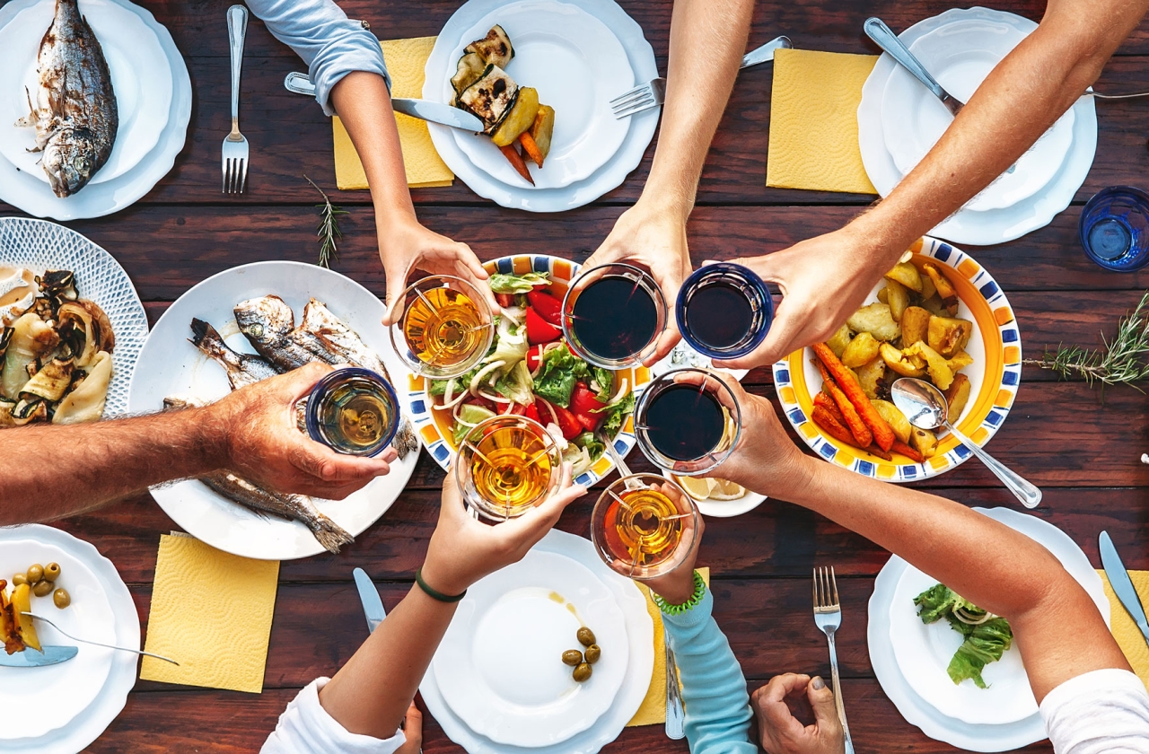 Hands clinking glasses on a table with food