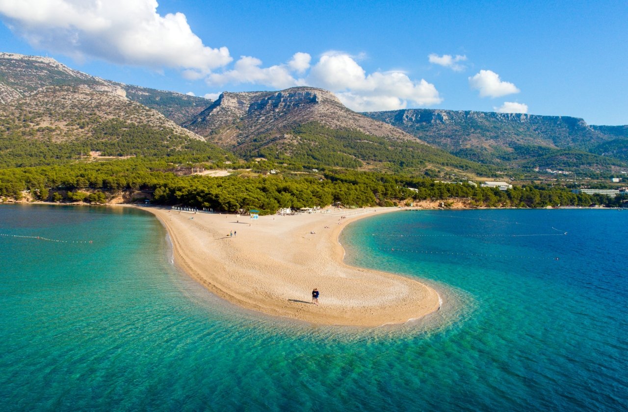 View of beach and blue waters on peninsula in Croatia with mountains in the background