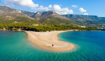 View of beach and blue waters on peninsula in Croatia with mountains in the background