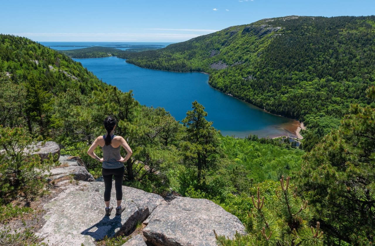 Hiker standing on a rock overlooking water and lush mountains at Acadia National Park, Maine