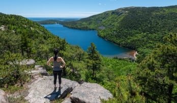 Hiker standing on a rock overlooking water and lush mountains at Acadia National Park, Maine