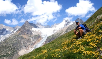 Hiker resting on a grassy hill with wildflowers and mountain views in the background, by Mont Blanc