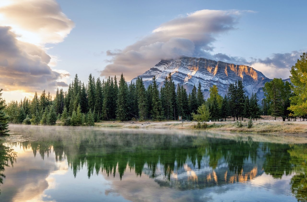 Early morning view of lake with mist rising on the surface and mountain views in the background, near Banff Canada