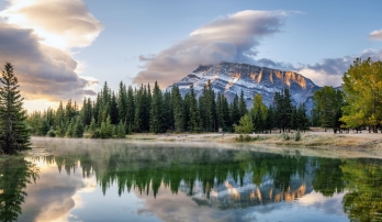 Early morning view of lake with mist rising on the surface and mountain views in the background, near Banff Canada