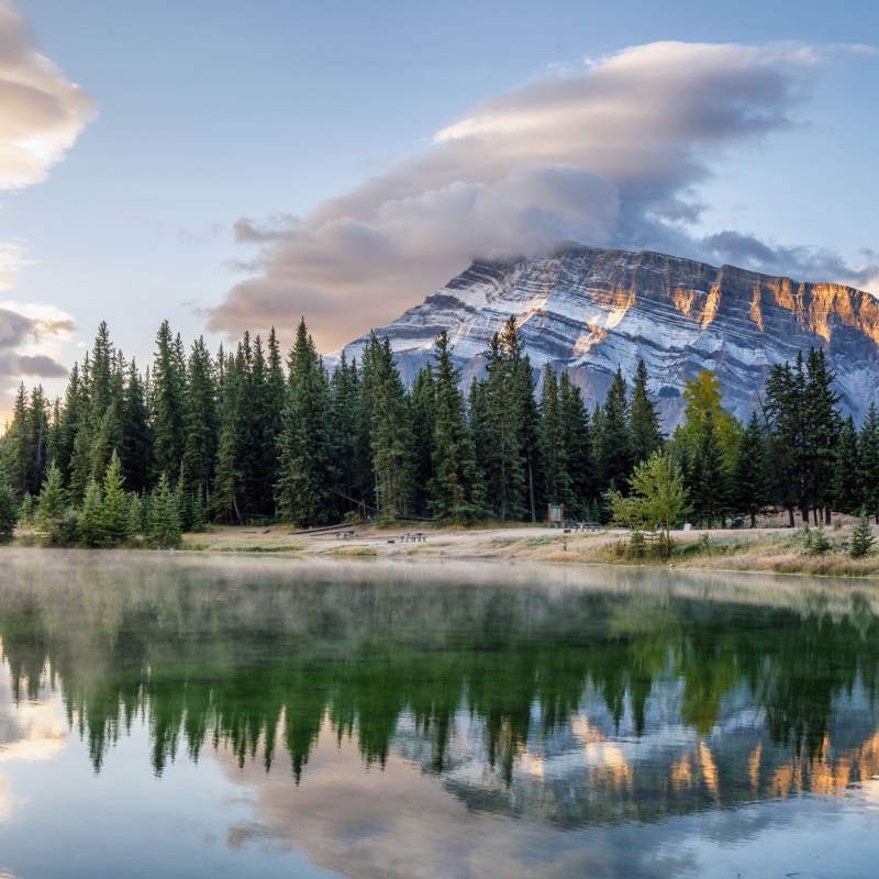 Early morning view of lake with mist rising on the surface and mountain views in the background, near Banff Canada