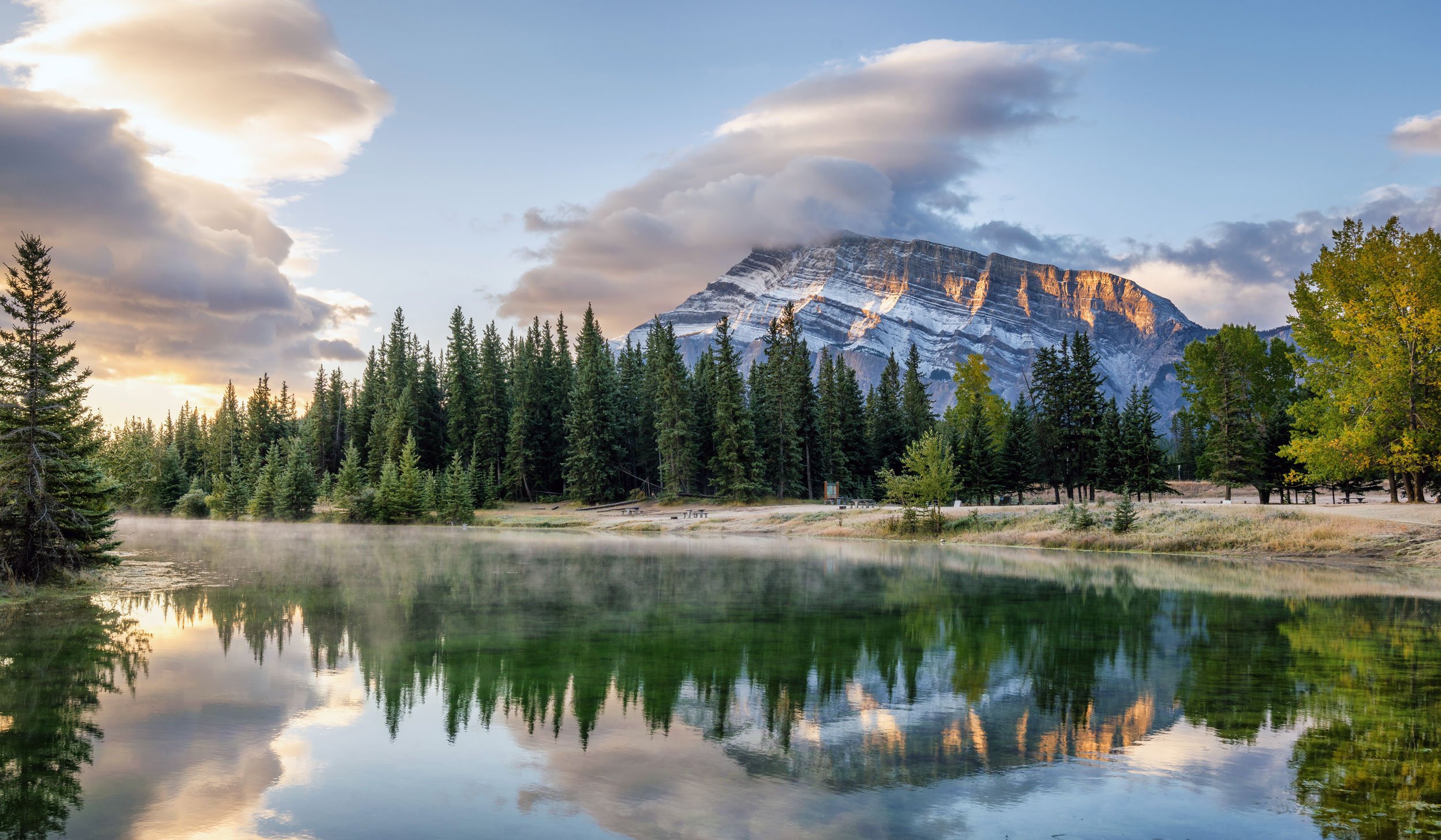 Early morning view of lake with mist rising on the surface and mountain views in the background, near Banff Canada